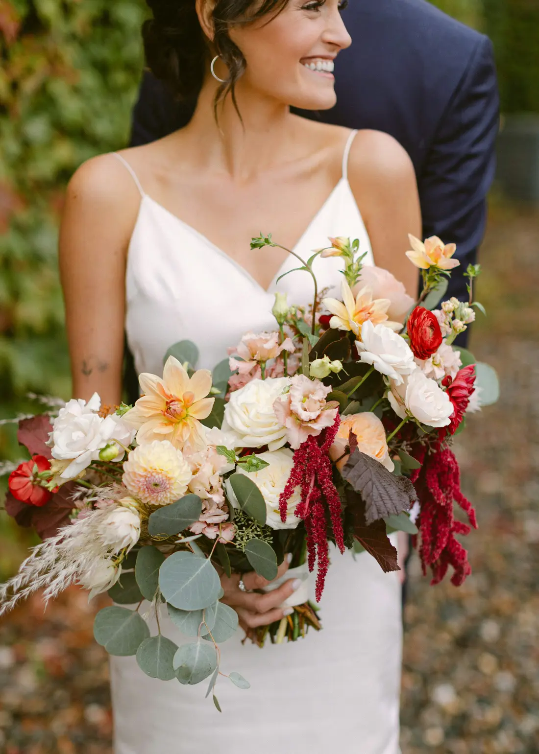 A bride holding a loose autumn bouquet of dahlias, roses and eucalyptus