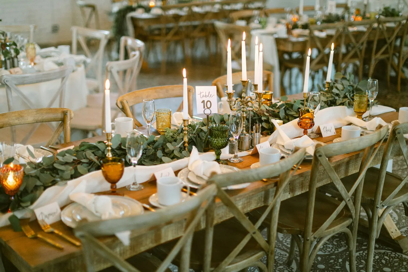 A pine farm table set with brass candlesticks and amber glass in the Freight Room