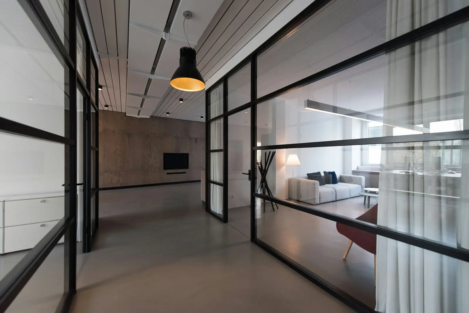 Steel-framed glass offices along a quiet corridor, a lamp left on in the far lounge, the concrete floor clean to the wall