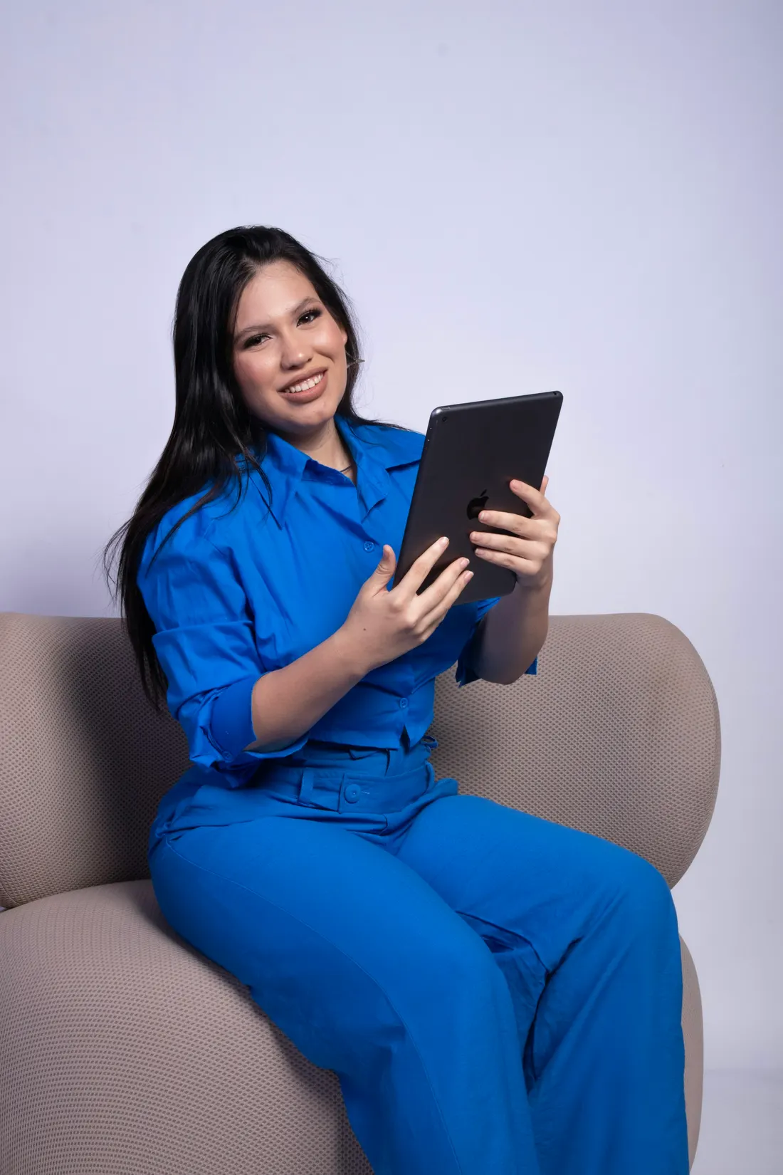 Dr. Inés Quintero in a cobalt suit, sitting on a sofa with a tablet