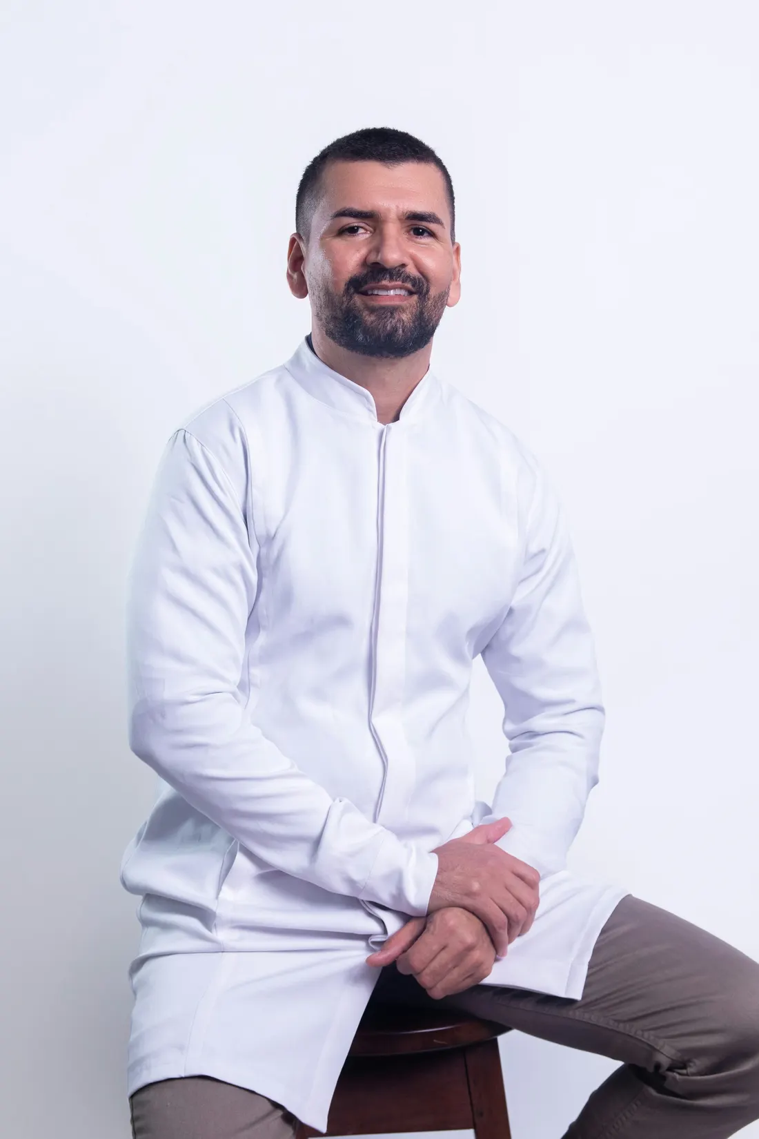 Dr. Tomás Ybarra in a white coat, sitting on a stool and smiling