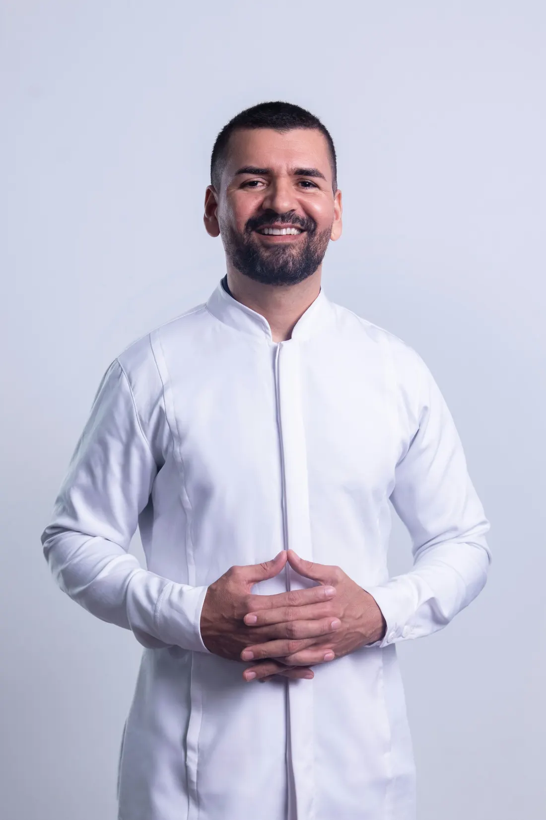 Dr. Tomás Ybarra in a white clinic coat, smiling, hands folded