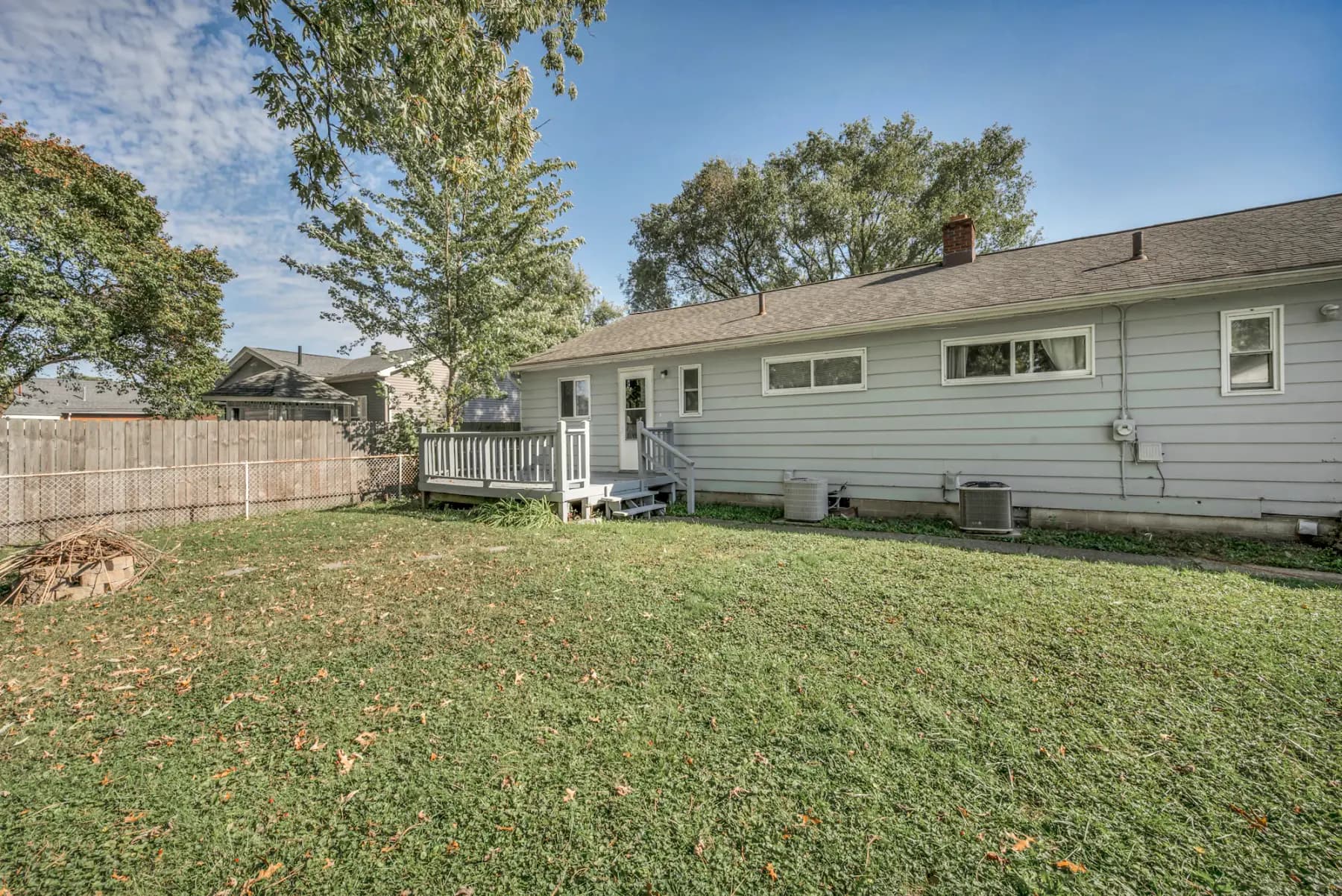 The back of a single-story grey ranch house with a small deck, two outdoor AC units against the wall and a wide lawn