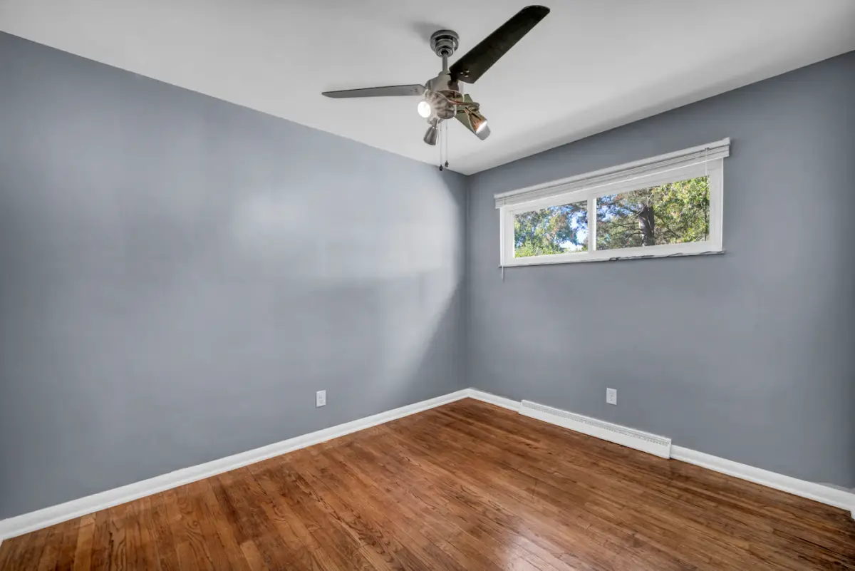 An empty bedroom with grey walls, oak floors and a ceiling fan