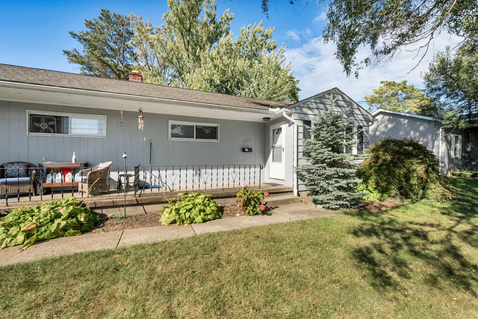 A grey single-story house with a covered front porch and a small evergreen in the yard