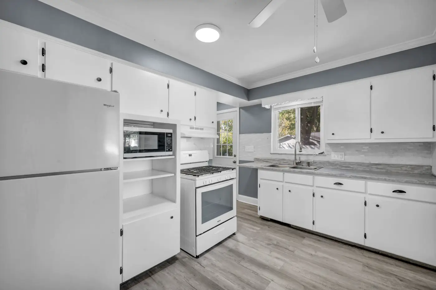 A small white kitchen with a white stove, fridge and cabinets under grey walls