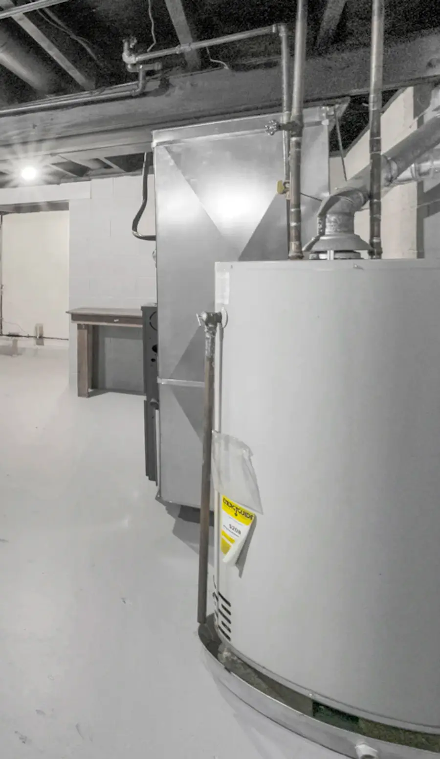 A gas furnace and a tank water heater side by side under exposed pipes